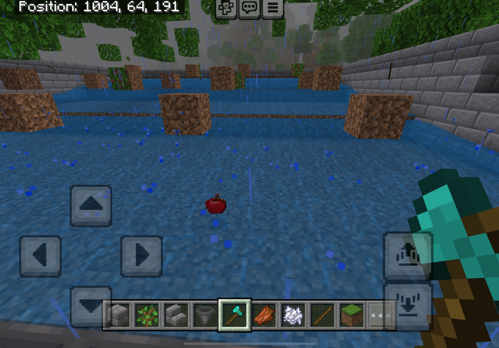 This image appears to be a screenshot from the game Minecraft. It shows a player holding a diamond axe while standing in a flooded area with multiple dirt blocks placed above the water surface. There's a red apple floating in the water, and it's raining in the game. The on-screen controls indicate this is a mobile version of the game. The position coordinates are displayed at the top, reading "Position: 1004, 64, 191.