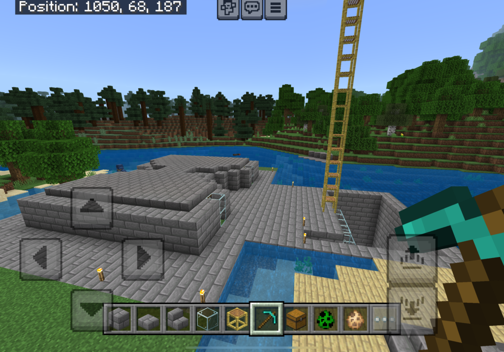 This image displays another Minecraft gameplay screenshot. It features a stone brick structure near a body of water, with a ladder extending high into the air. The surrounding area includes a river or lake and a forested landscape with trees. The user interface at the bottom shows various items, such as stone blocks, glass, a ladder, a chest, and a diamond pickaxe selected. The coordinates at the top indicate the position: 1050, 68, 187.